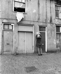 858796 Afbeelding van een medewerker van de gemeentelijke Bouw- en Woningdienst die een bordje onbewoonbaar verklaarde ...